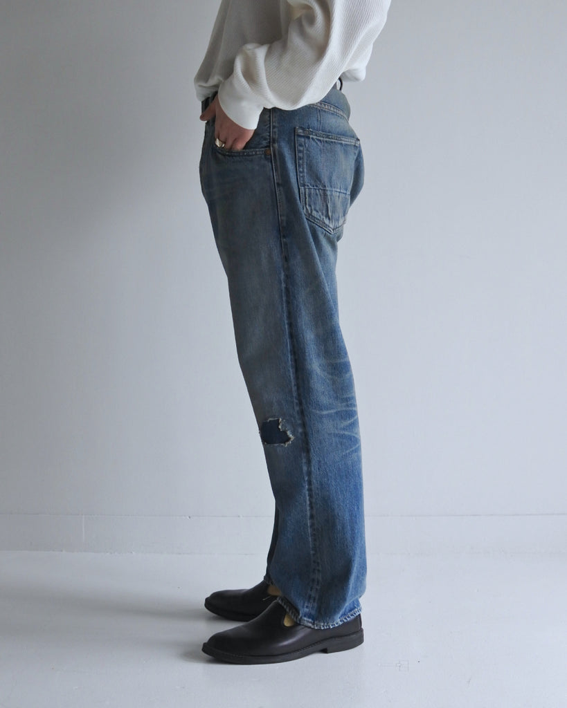 腰回りにゆとりを持たせ、裾を絞ったレギュラーテーパードの5Pパンツ。旧式力織機による12.5ozセルビッチデニムを使用しました。5年間の激しい着用を想定した加工に加え、ダメージリペアと最終工程の汚し加工を施すことで、長年愛用されたヴィンテージの風格を圧倒的なリアリティで再現したリメイクモデルです。

Regular tapered 5P pants in 12.5oz selvedge denim. The "Five Year" finish features heavy fading and bold wear patterns, enhanced by meticulous repair work and a final "dirt" tint for a realistic vintage feel. These remade pants capture the rugged essence of long-term wear with an authentic, street-ready character.