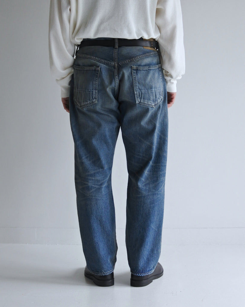 腰回りにゆとりを持たせ、裾を絞ったレギュラーテーパードの5Pパンツ。旧式力織機による12.5ozセルビッチデニムを使用しました。5年間の激しい着用を想定した加工に加え、ダメージリペアと最終工程の汚し加工を施すことで、長年愛用されたヴィンテージの風格を圧倒的なリアリティで再現したリメイクモデルです。

Regular tapered 5P pants in 12.5oz selvedge denim. The "Five Year" finish features heavy fading and bold wear patterns, enhanced by meticulous repair work and a final "dirt" tint for a realistic vintage feel. These remade pants capture the rugged essence of long-term wear with an authentic, street-ready character.